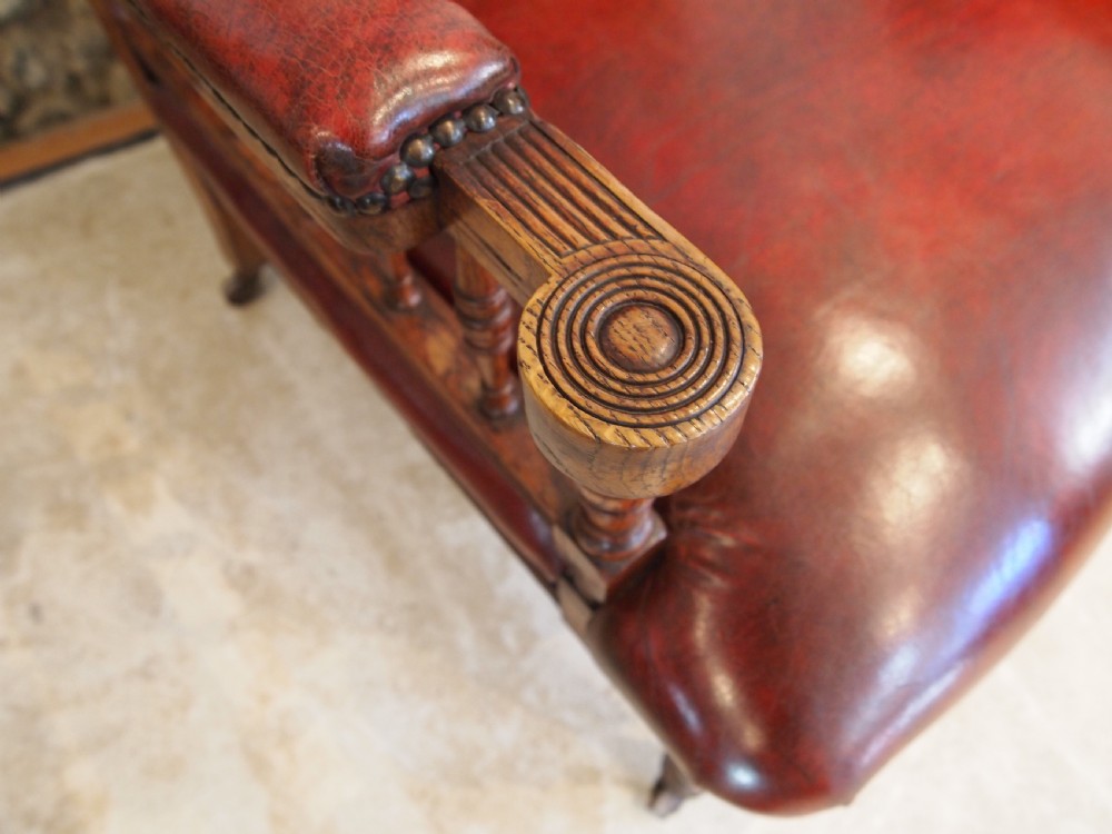 An early Victorian oak armchair with button-tufted chestnut brown leather upholstery, spindled arm supports, turned front legs, and brass casters. View II