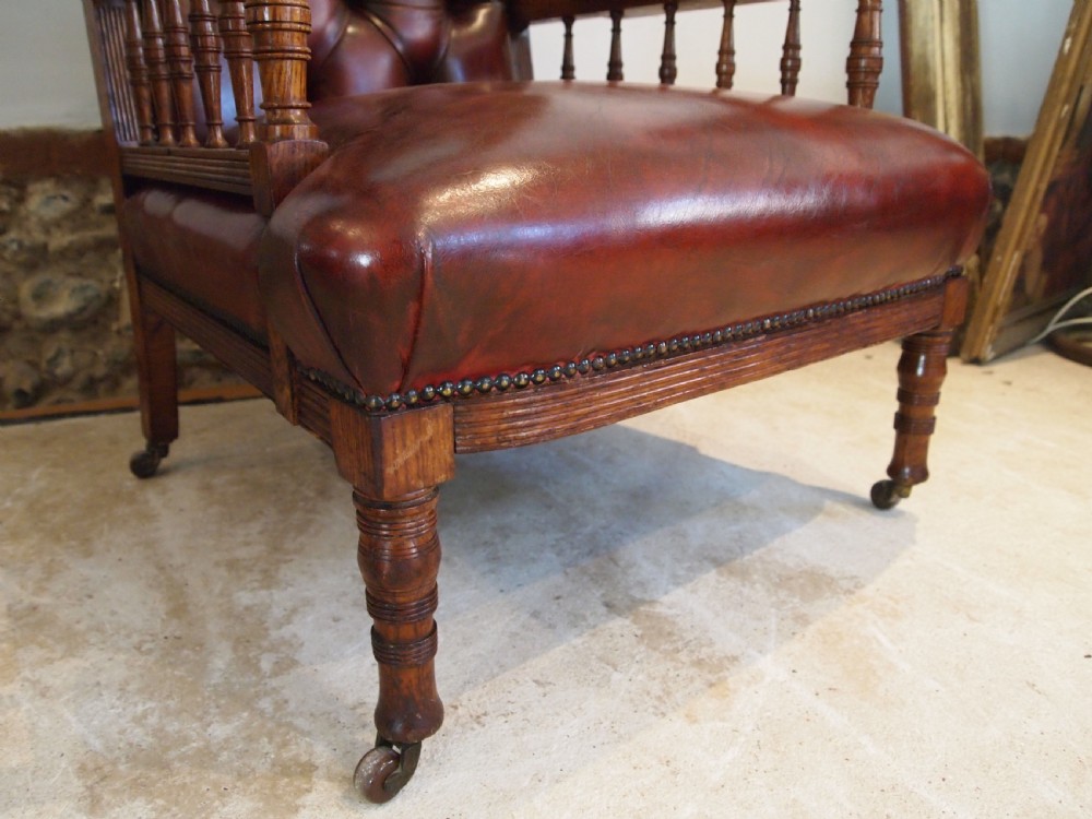 An early Victorian oak armchair with button-tufted chestnut brown leather upholstery, spindled arm supports, turned front legs, and brass casters. View IV