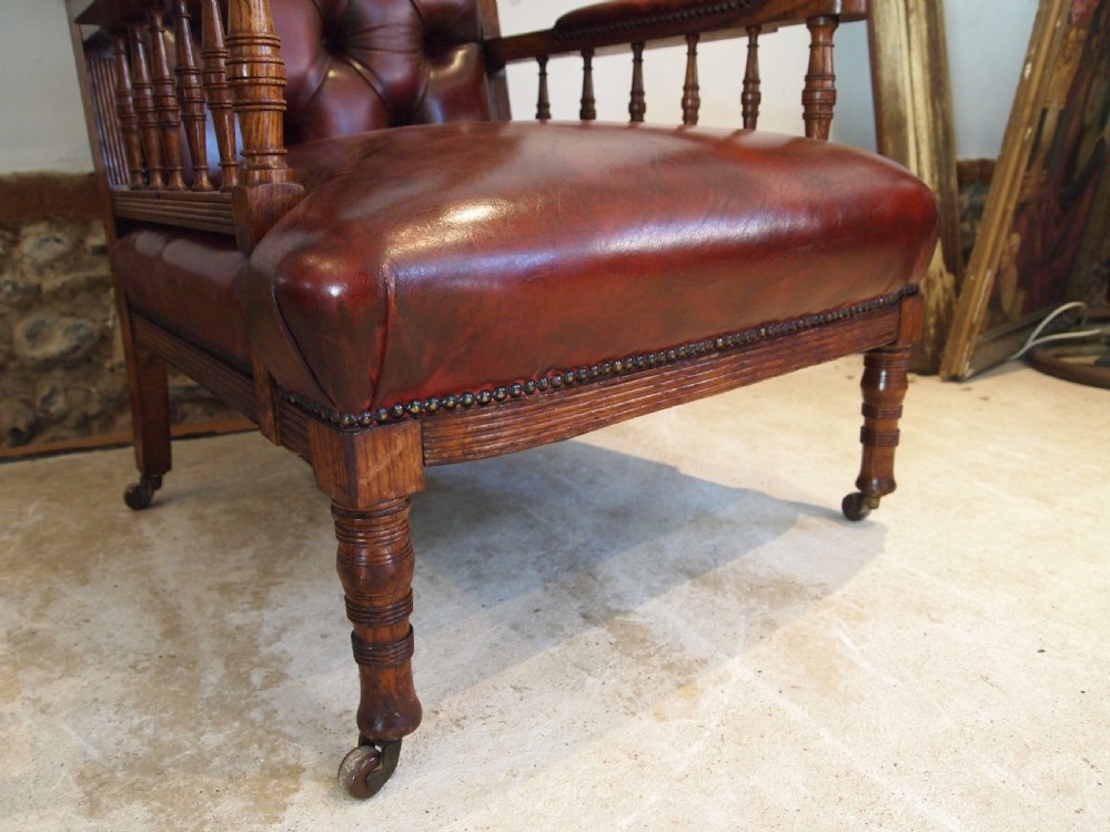 An early Victorian oak armchair with button-tufted chestnut brown leather upholstery, spindled arm supports, turned front legs, and brass casters. View VII