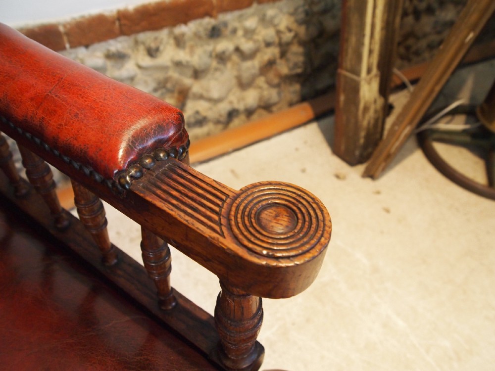 An early Victorian oak armchair with button-tufted chestnut brown leather upholstery, spindled arm supports, turned front legs, and brass casters. View VIII
