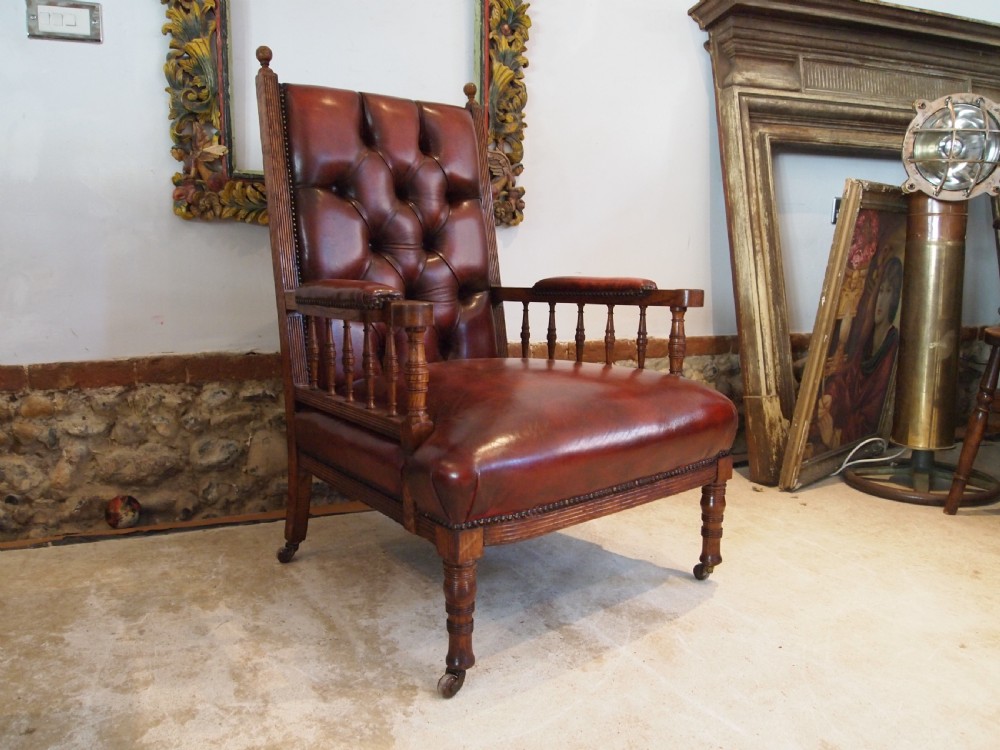 An early Victorian oak armchair with button-tufted chestnut brown leather upholstery, spindled arm supports, turned front legs, and brass casters. View X