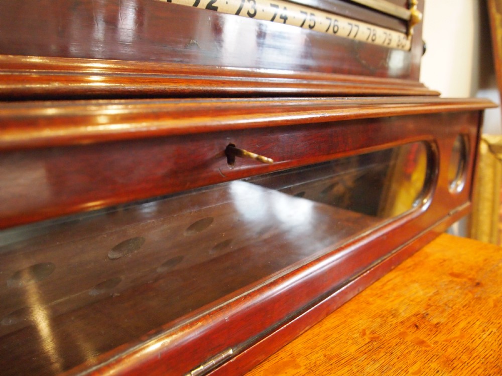 A Victorian mahogany snooker scoreboard featuring brass tracking rails, numbered rollers, a central chalkboard, and a glass-fronted lower cabinet. View VI