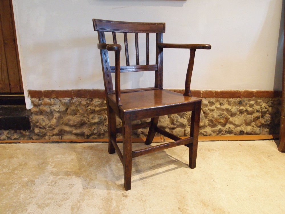 A George IV period dark elm Windsor armchair featuring a rectangular top rail, vertical back splats, shaped armrests, a solid seat, and square legs joined by stretchers.