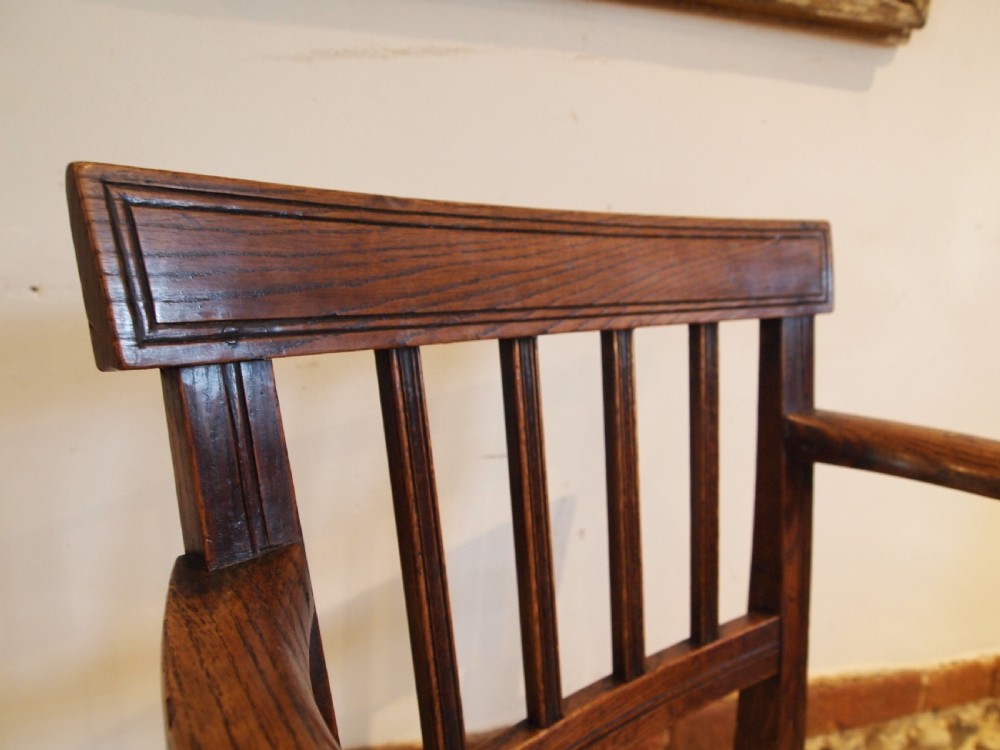 A George IV period dark elm Windsor armchair featuring a rectangular top rail, vertical back splats, shaped armrests, a solid seat, and square legs joined by stretchers. View II