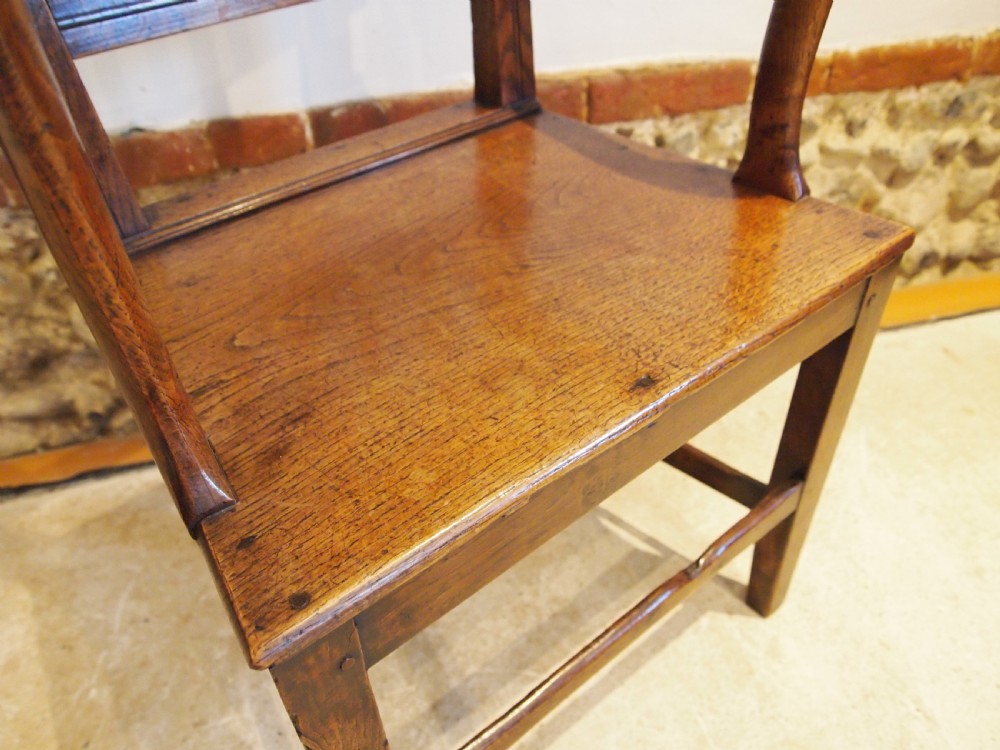 A George IV period dark elm Windsor armchair featuring a rectangular top rail, vertical back splats, shaped armrests, a solid seat, and square legs joined by stretchers. View III