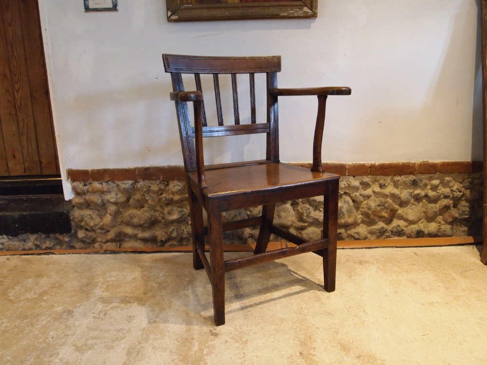 A George IV period dark elm Windsor armchair featuring a rectangular top rail, vertical back splats, shaped armrests, a solid seat, and square legs joined by stretchers. View X