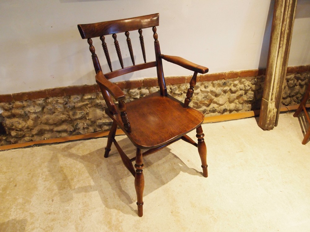 A Victorian wooden Windsor armchair with turned back spindles, shaped armrests, a solid timber seat, and turned legs.
