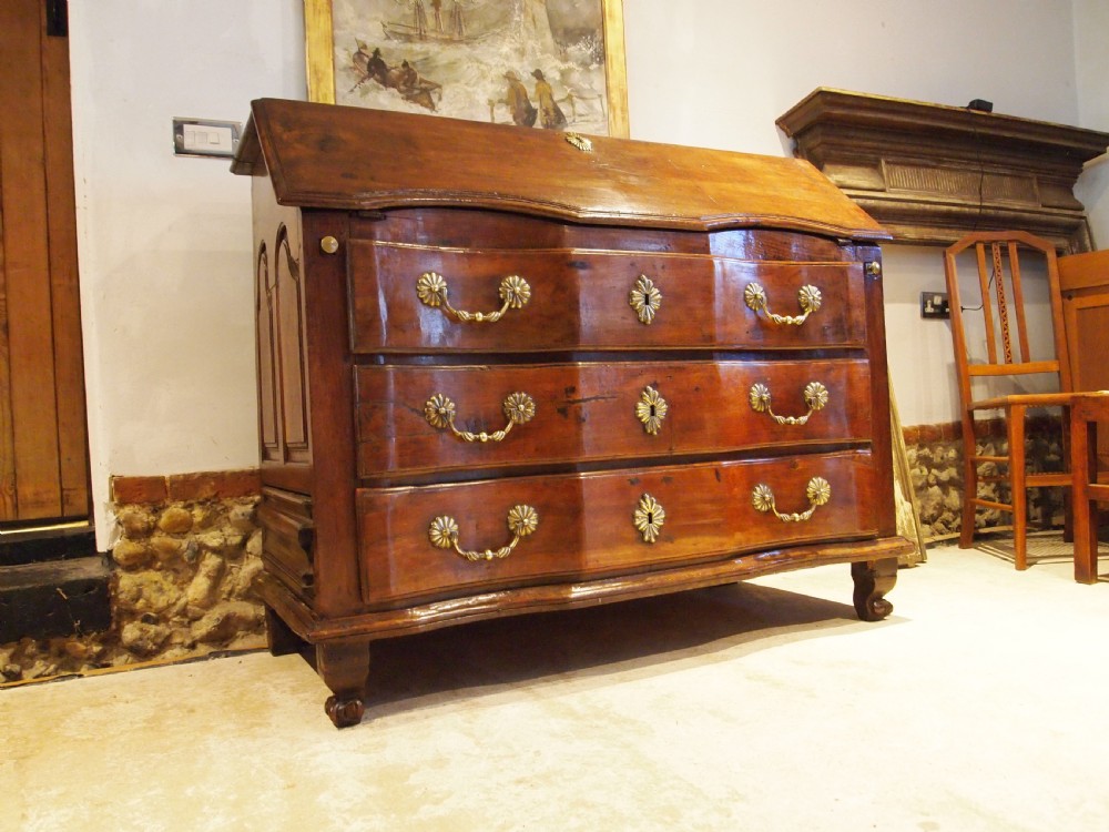 An 18th-century French walnut slant-front bureau desk featuring three wide drawers with ornamental brass handles and keyhole escutcheons.