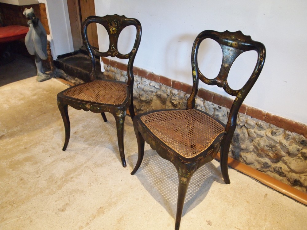 A pair of black Victorian side chairs featuring hand-painted floral details, balloon backrests, and woven cane seats.