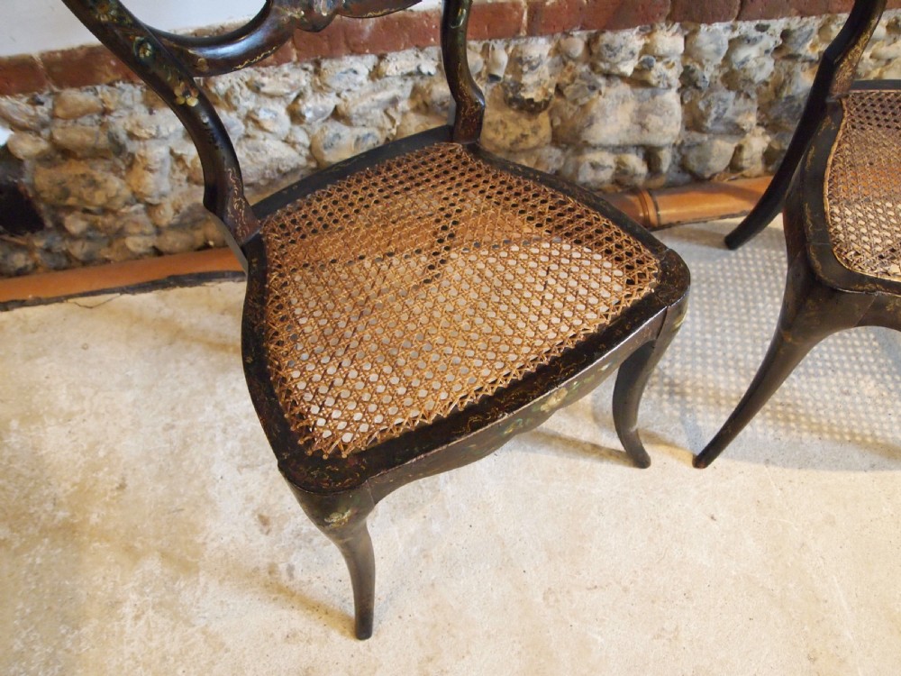 A pair of black Victorian side chairs featuring hand-painted floral details, balloon backrests, and woven cane seats. View V