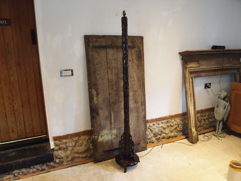 A tall early 20th-century Burmese standard lamp crafted from dark padouk wood, featuring intricate high-relief carving along the entire column and base.