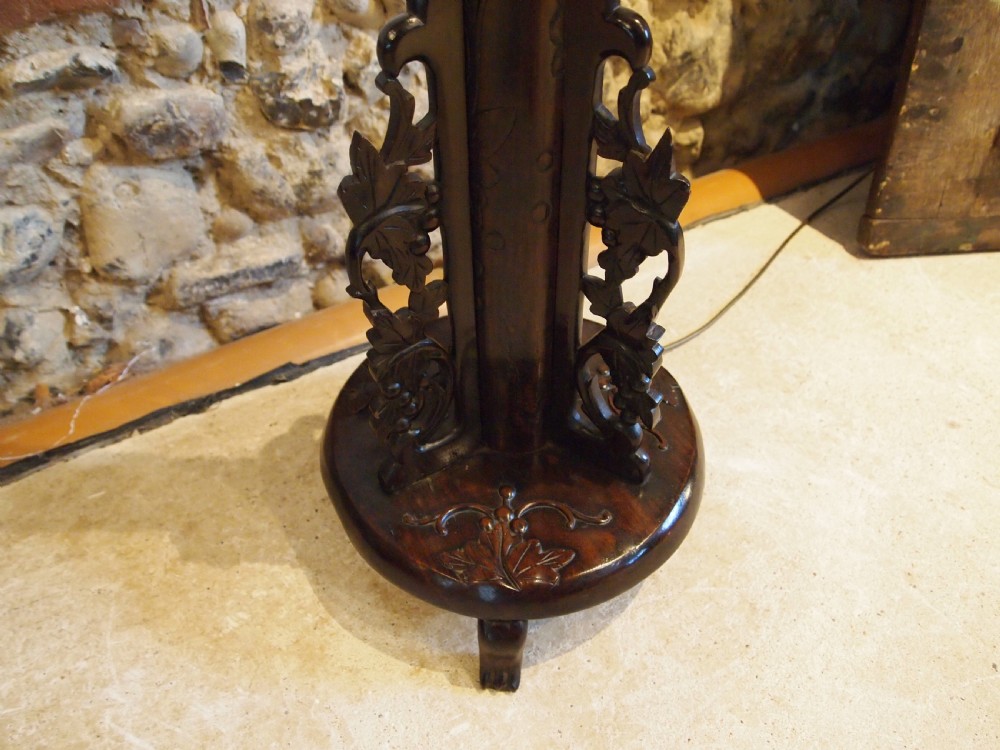 A tall early 20th-century Burmese standard lamp crafted from dark padouk wood, featuring intricate high-relief carving along the entire column and base. View II