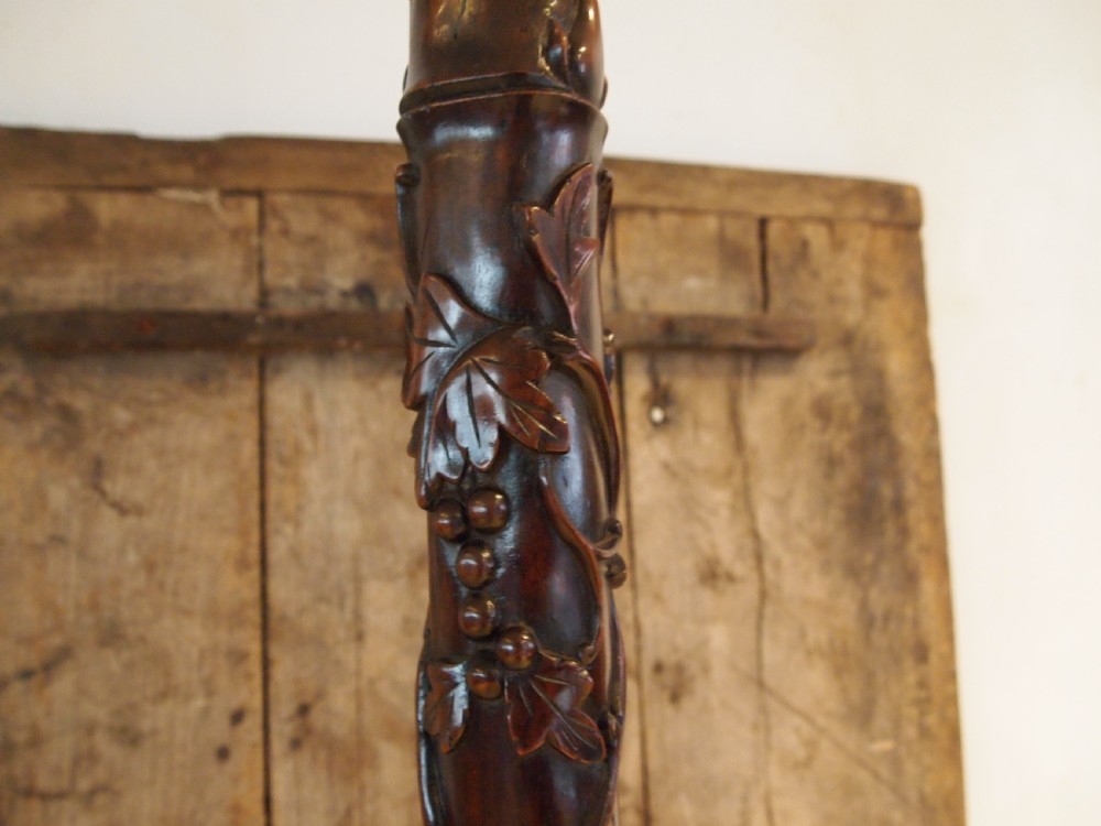 A tall early 20th-century Burmese standard lamp crafted from dark padouk wood, featuring intricate high-relief carving along the entire column and base. View III