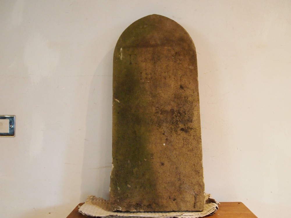 A weathered Victorian York stone headstone with an arched top, featuring carved initials and the date 1868.