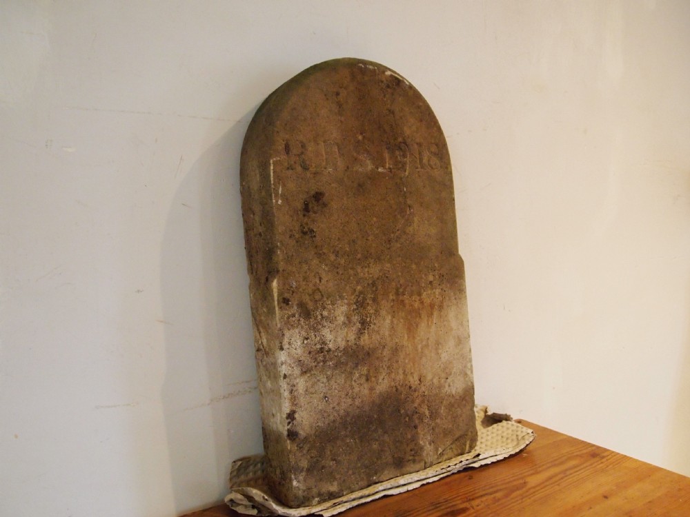 An arched top York stone headstone dated 1918 with hand-carved initials and weathered buff surface.
