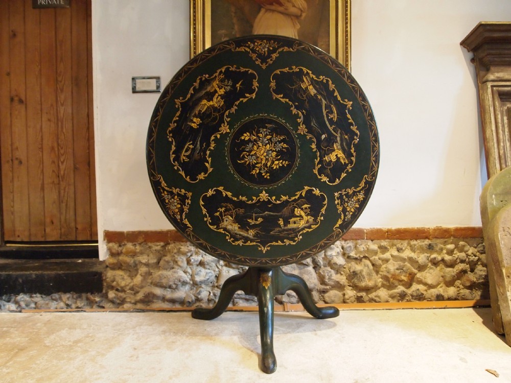 A circular black lacquered tilt-top table featuring intricate gold gilt Chinoiserie cartouches resting on a tripod pedestal base. View II