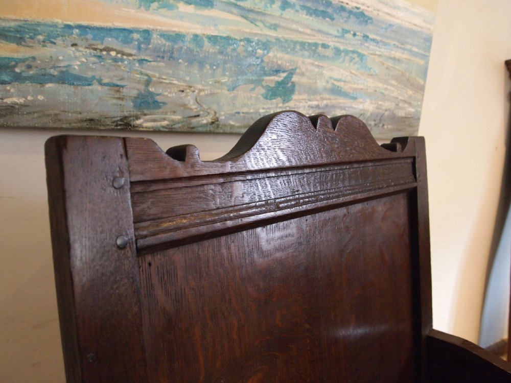 An early 18th-century dark oak lambing chair featuring a high panelled back, enclosed box base, integrated shaped arms, and a cut crest rail. View III