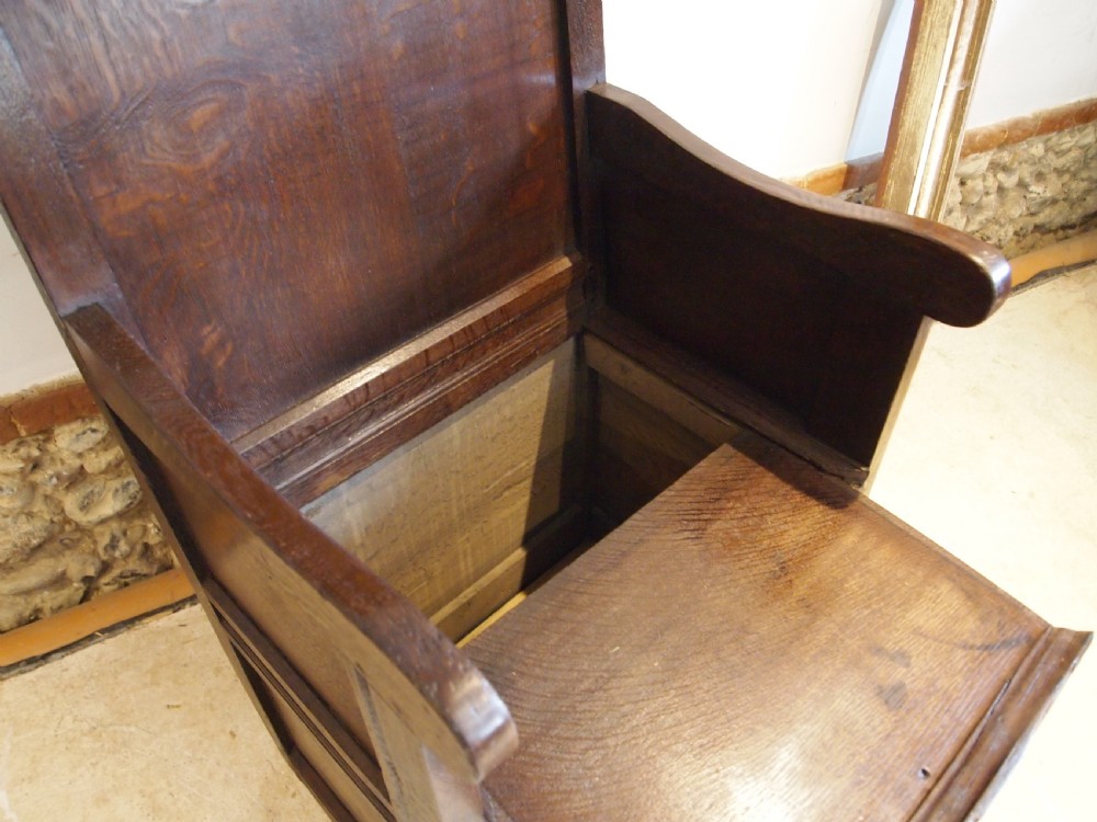 An early 18th-century dark oak lambing chair featuring a high panelled back, enclosed box base, integrated shaped arms, and a cut crest rail. View V