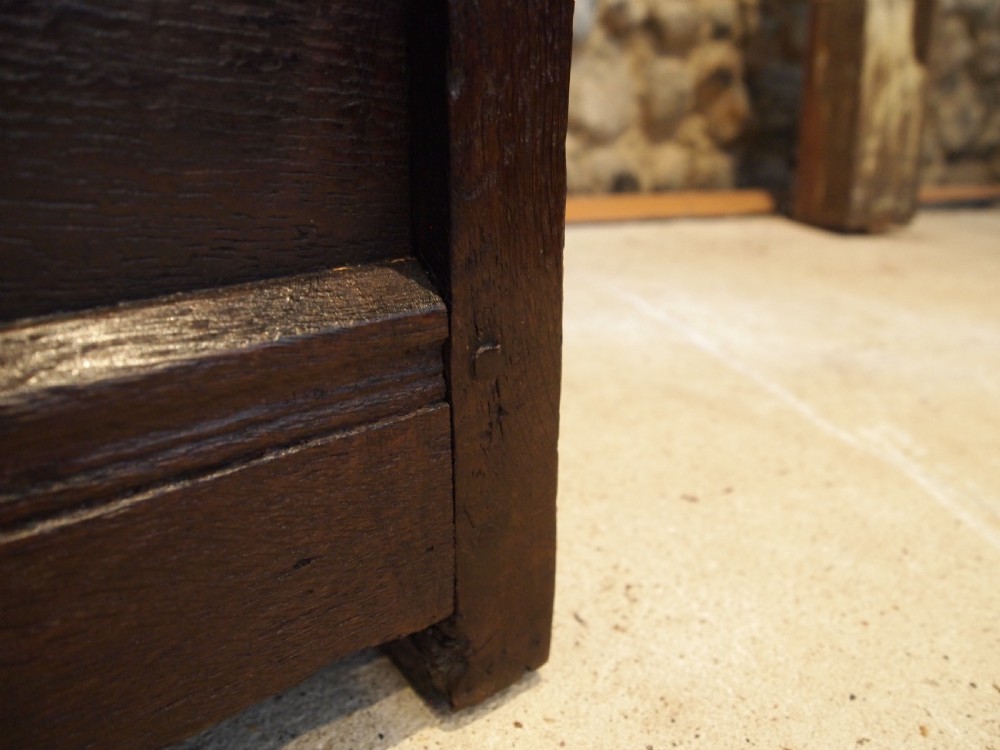 An early 18th-century dark oak lambing chair featuring a high panelled back, enclosed box base, integrated shaped arms, and a cut crest rail. View XII