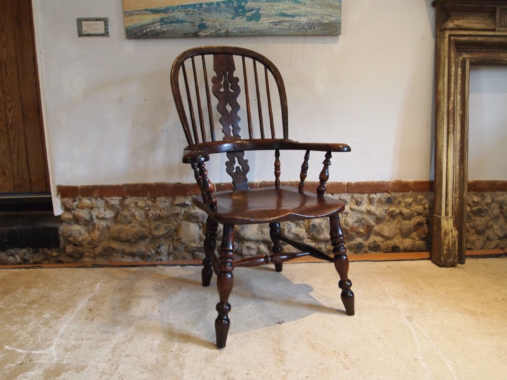 An antique 19th-century yew wood Windsor armchair featuring a bowed top rail, pierced central splat, turned spindles, armrests, and turned legs joined by an H-stretcher.