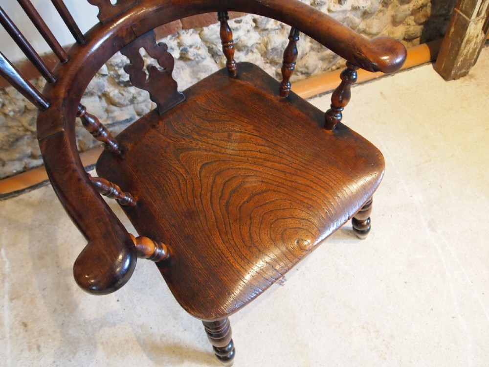 An antique 19th-century yew wood Windsor armchair featuring a bowed top rail, pierced central splat, turned spindles, armrests, and turned legs joined by an H-stretcher. View X