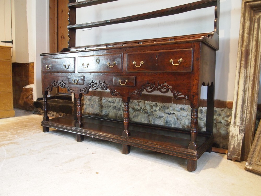 An 18th-century Welsh oak potboard dresser featuring an open plate rack, small upper drawers, a base with main drawers, shaped aprons, and turned legs. View II