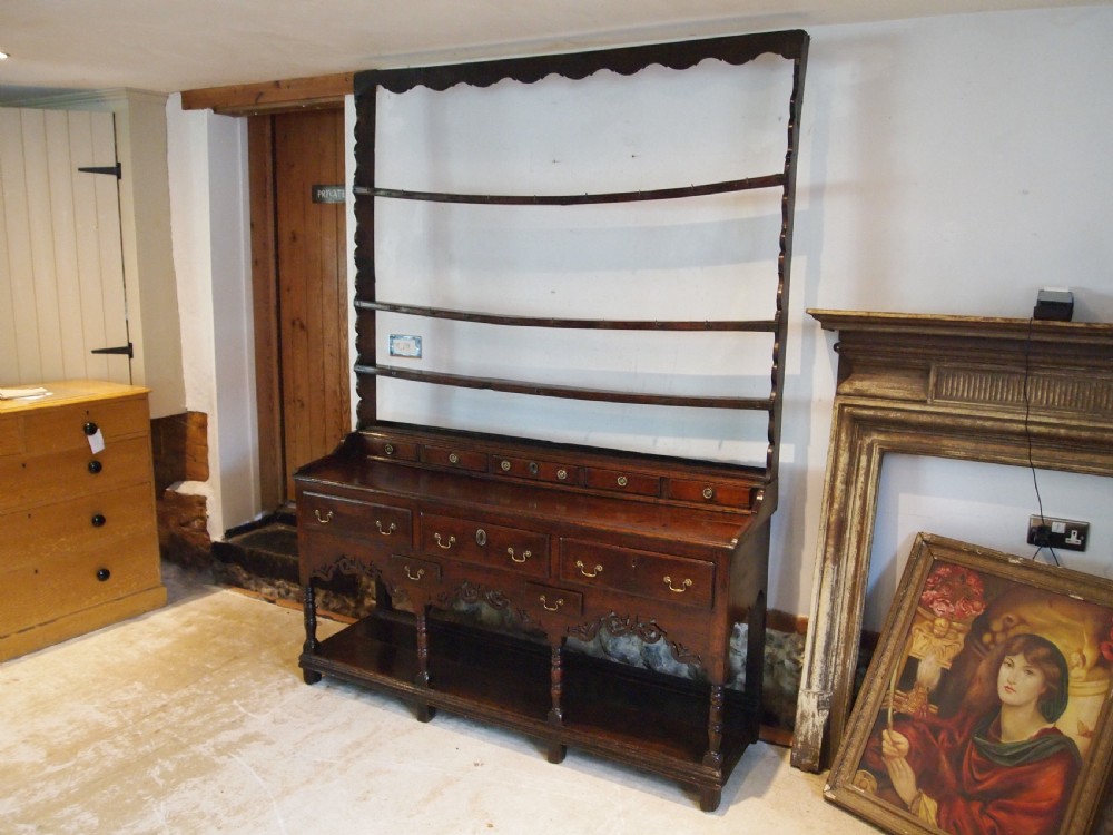 An 18th-century Welsh oak potboard dresser featuring an open plate rack, small upper drawers, a base with main drawers, shaped aprons, and turned legs.