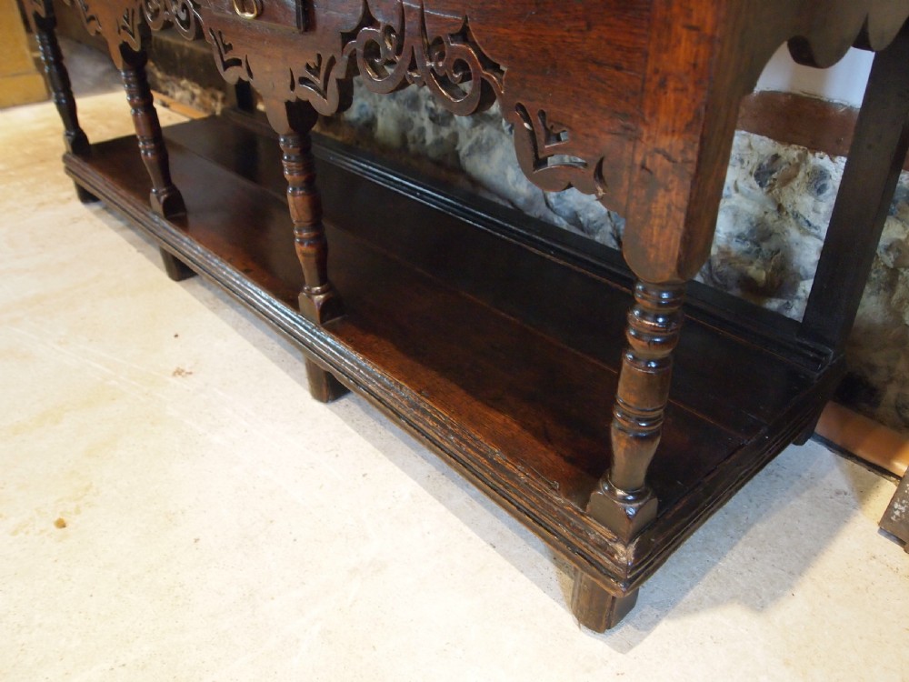 An 18th-century Welsh oak potboard dresser featuring an open plate rack, small upper drawers, a base with main drawers, shaped aprons, and turned legs. View VII