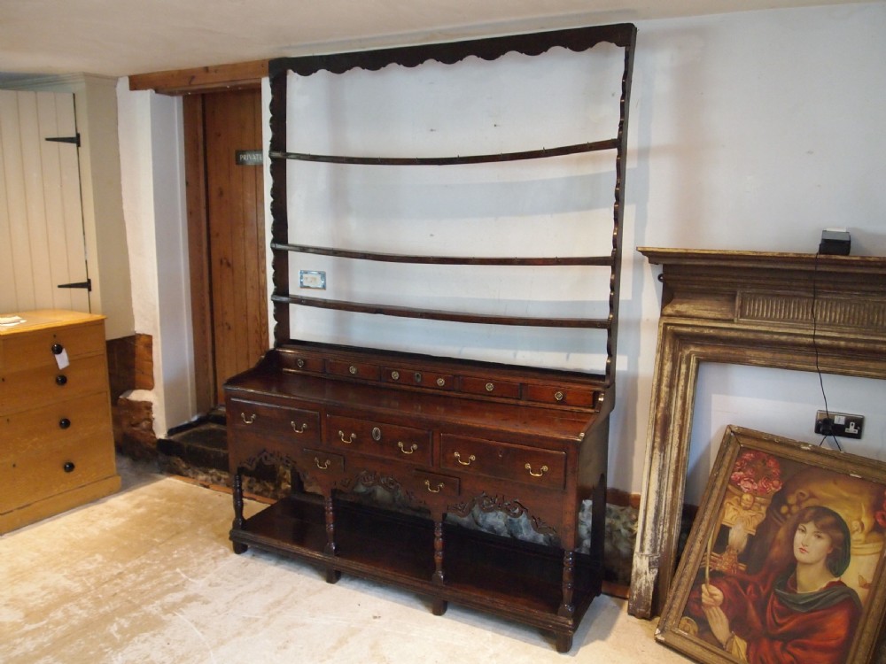 An 18th-century Welsh oak potboard dresser featuring an open plate rack, small upper drawers, a base with main drawers, shaped aprons, and turned legs. View VIII