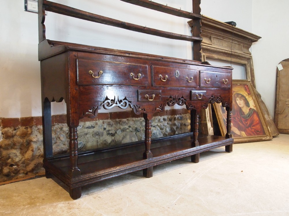 An 18th-century Welsh oak potboard dresser featuring an open plate rack, small upper drawers, a base with main drawers, shaped aprons, and turned legs. View XI