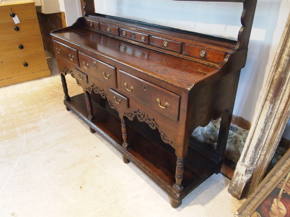 An 18th-century Welsh oak potboard dresser featuring an open plate rack, small upper drawers, a base with main drawers, shaped aprons, and turned legs. View XII