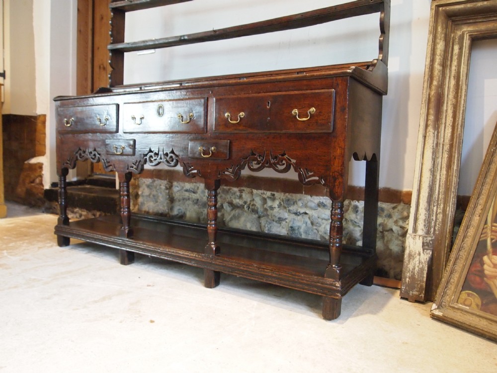 An 18th-century Welsh oak potboard dresser featuring an open plate rack, small upper drawers, a base with main drawers, shaped aprons, and turned legs. View XIII