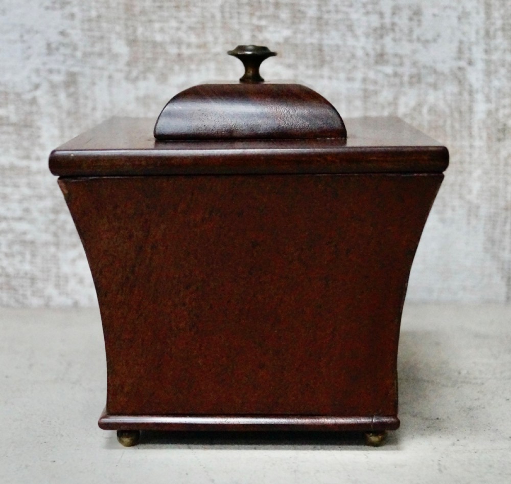 A mahogany sarcophagus-shaped tea caddy featuring flared sides, a stepped hinged lid with a central brass finial, and small brass feet. View II