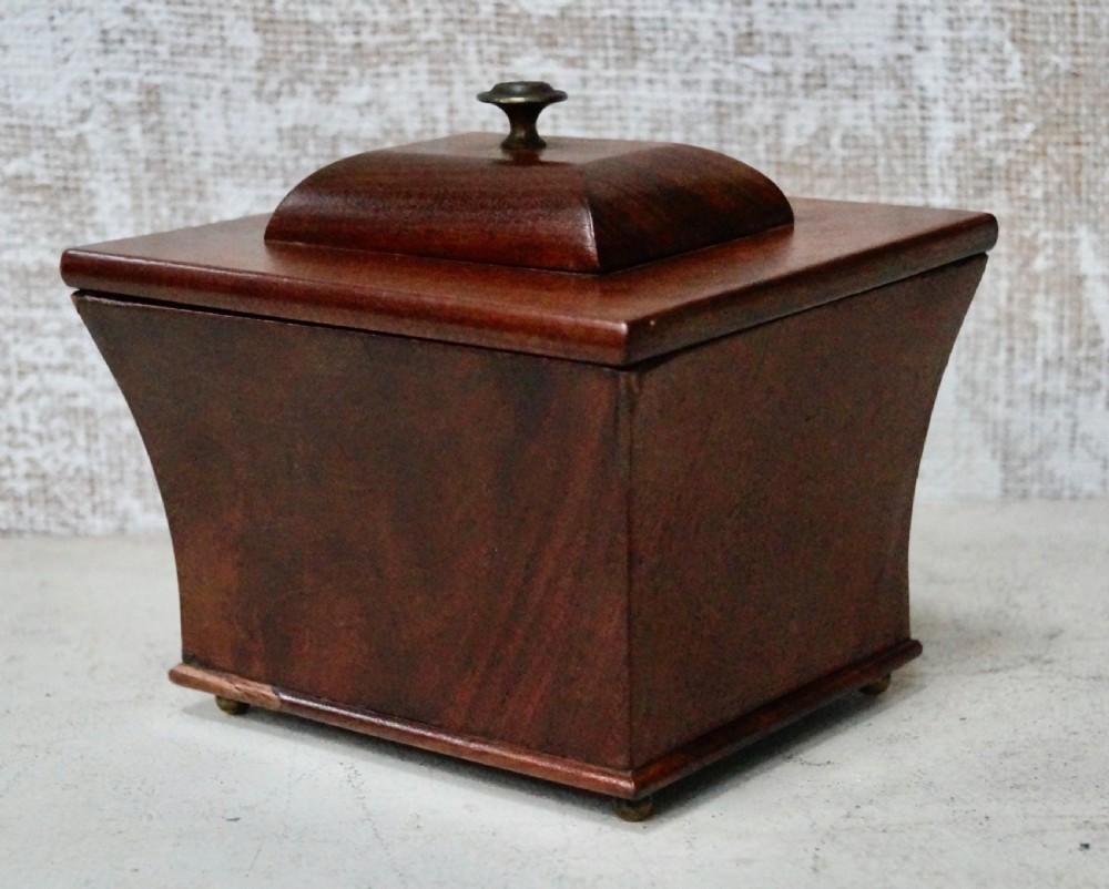 A mahogany sarcophagus-shaped tea caddy featuring flared sides, a stepped hinged lid with a central brass finial, and small brass feet. View III