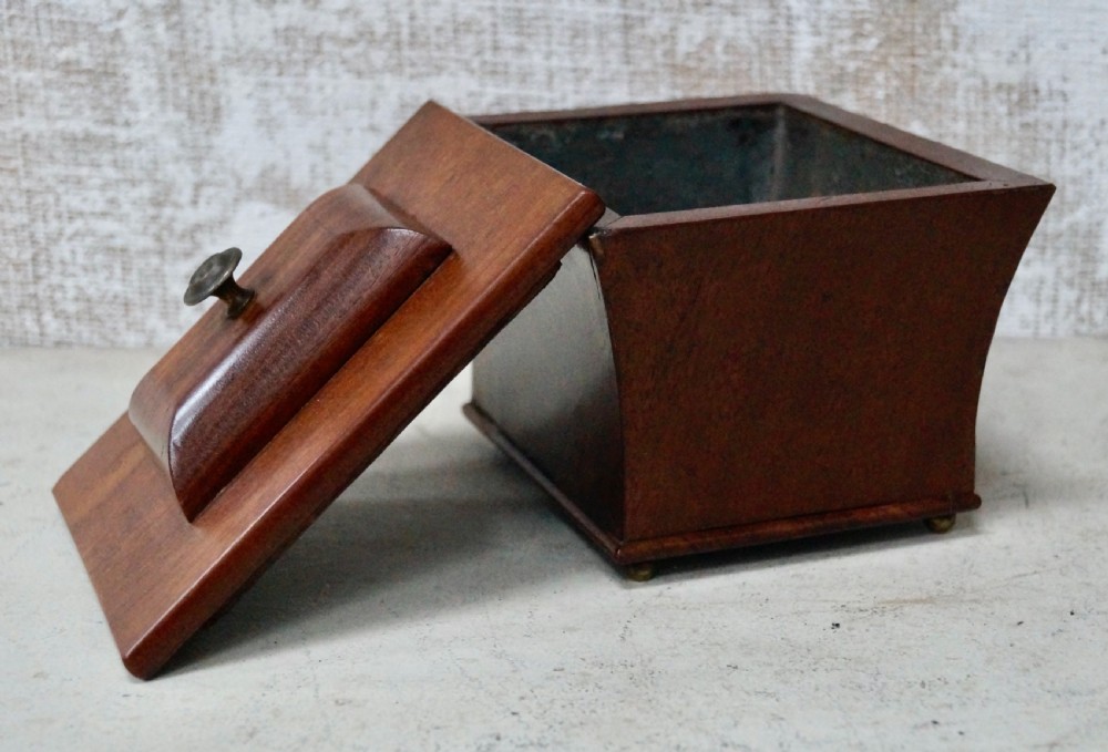 A mahogany sarcophagus-shaped tea caddy featuring flared sides, a stepped hinged lid with a central brass finial, and small brass feet. View V