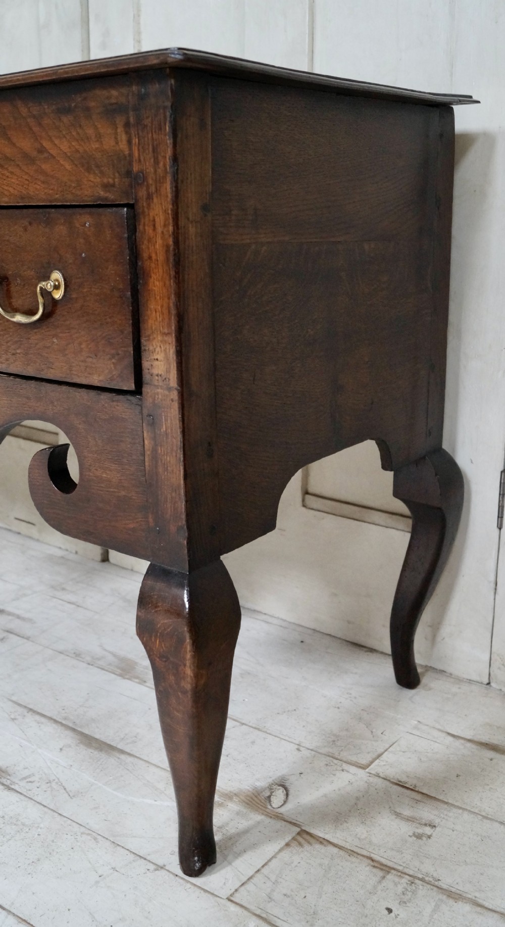 An early Georgian dark oak dresser base featuring three drawers with brass handles, a distinctive scrolled apron, and cabriole legs. View III