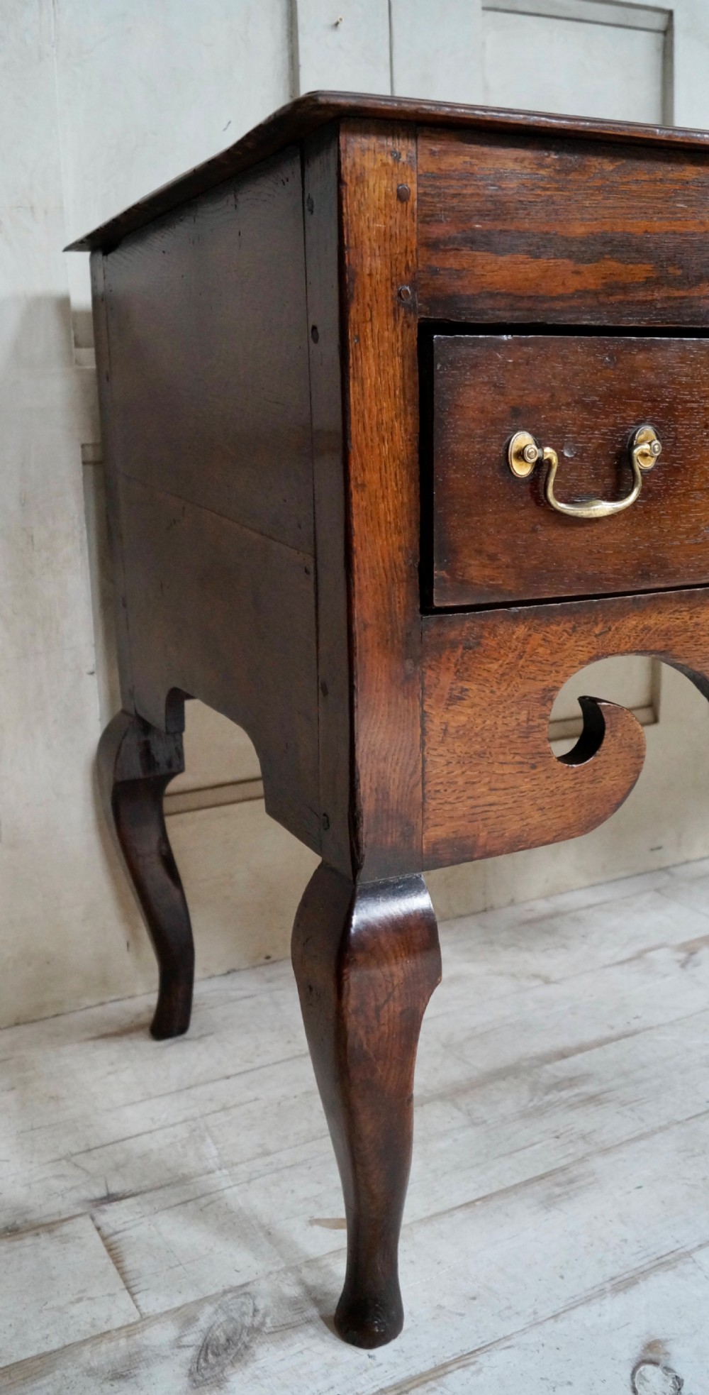 An early Georgian dark oak dresser base featuring three drawers with brass handles, a distinctive scrolled apron, and cabriole legs. View VI