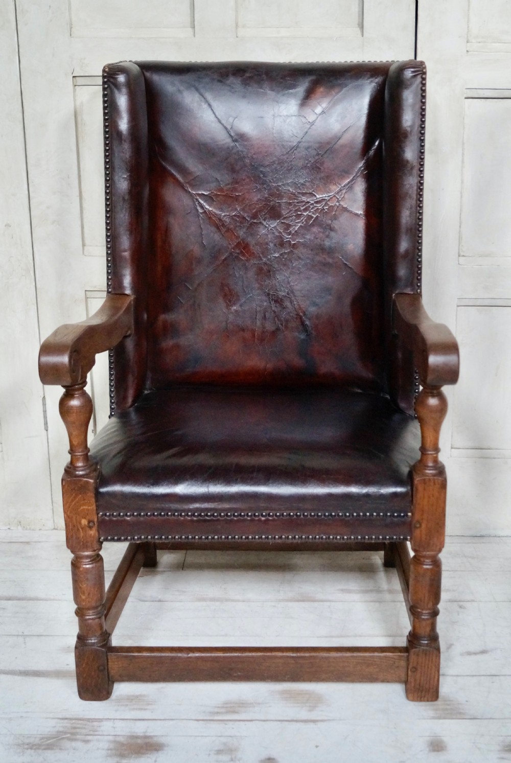A Victorian library chair featuring dark brown aged leather upholstery with studding detail and a solid oak frame with turned front legs.