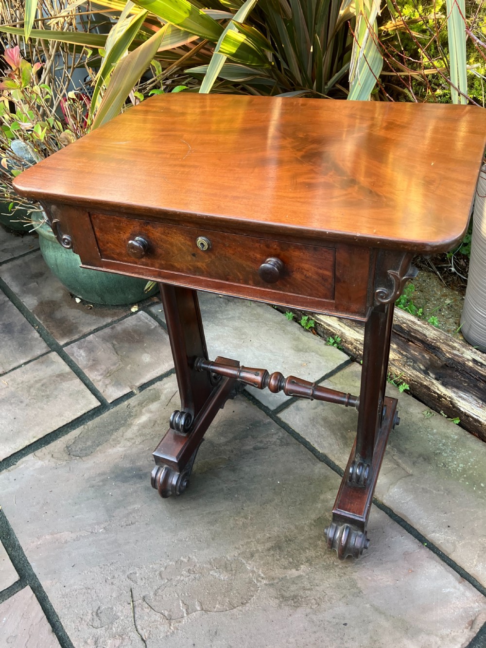 A William IV mahogany side table featuring a single drawer with turned knobs, resting on turned trestle supports and scroll feet.