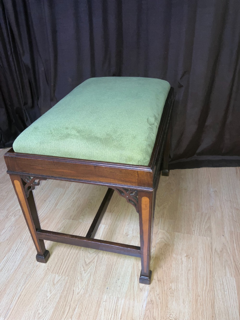 An Edwardian mahogany rectangular stool with light wood inlay on tapered legs, corner fretwork spandrels, an H-stretcher, and a green upholstered seat. View III