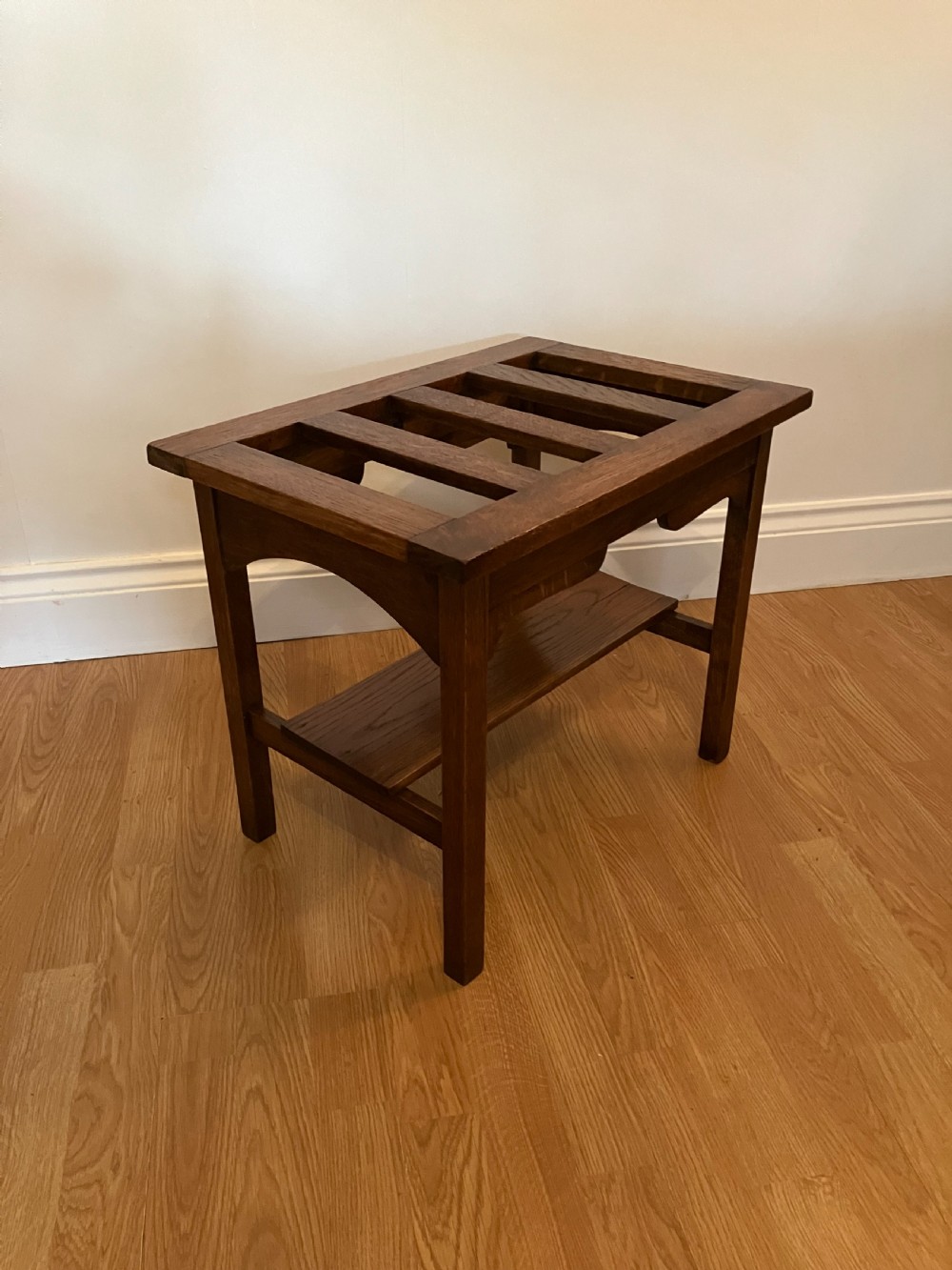 A dark oak luggage rack featuring a slatted top surface, lower shelf tier, rectangular frame, and square legs.
