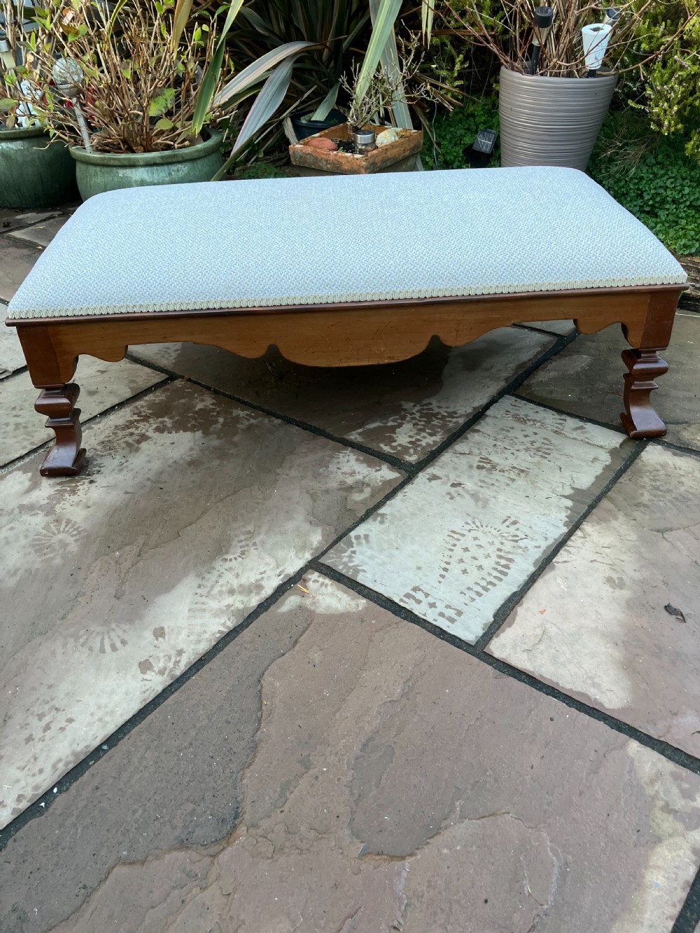 A low rectangular Victorian mahogany footstool upholstered in pale blue fabric with a shaped apron and turned legs.
