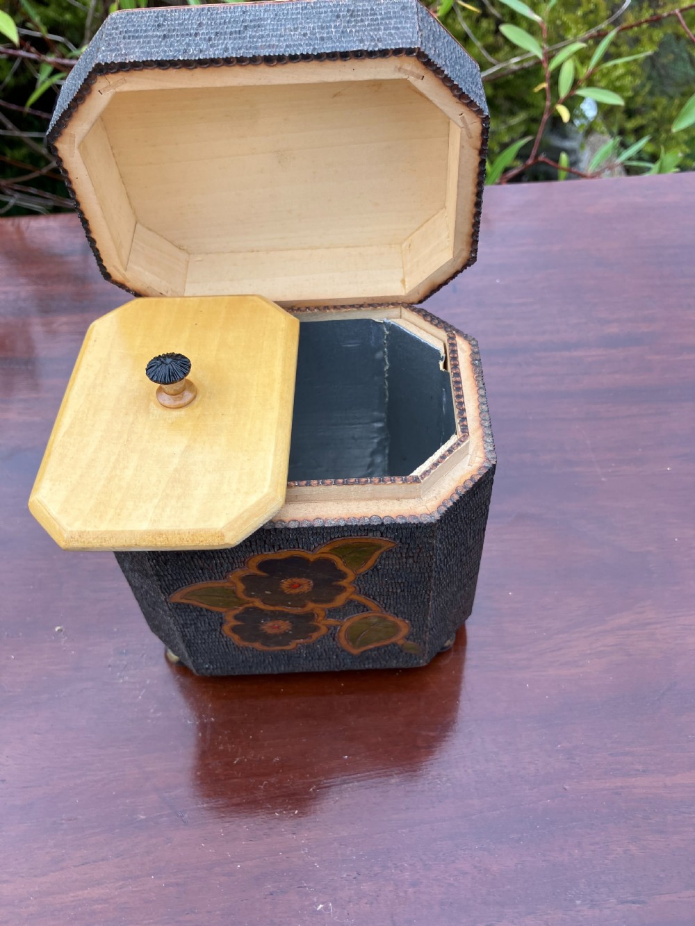 An octagonal wooden tea caddy featuring a textured stippled dark brown body, small brass feet, and painted yellow and red floral designs on the lid and front panel. View II