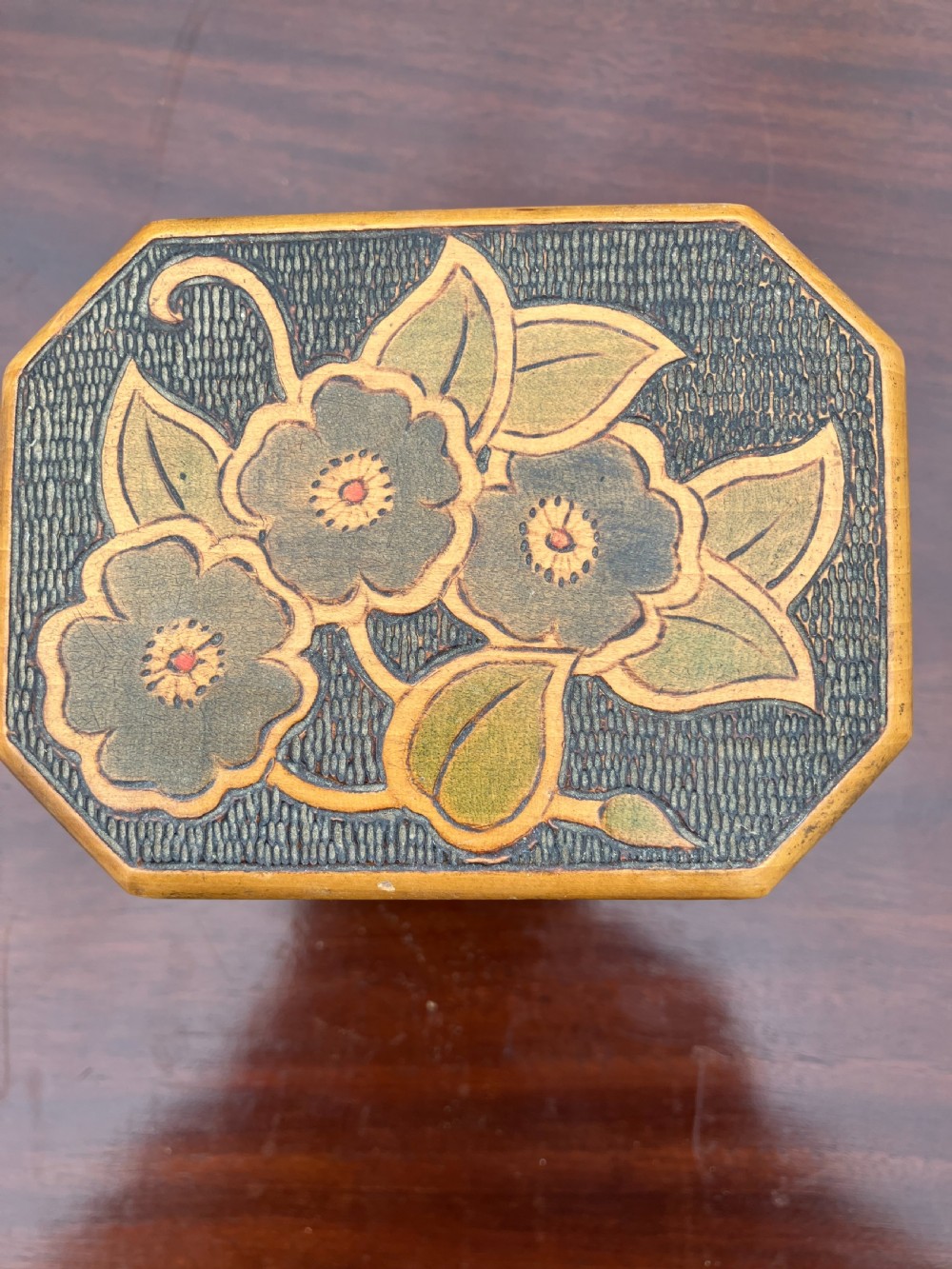 An octagonal wooden tea caddy featuring a textured stippled dark brown body, small brass feet, and painted yellow and red floral designs on the lid and front panel. View III