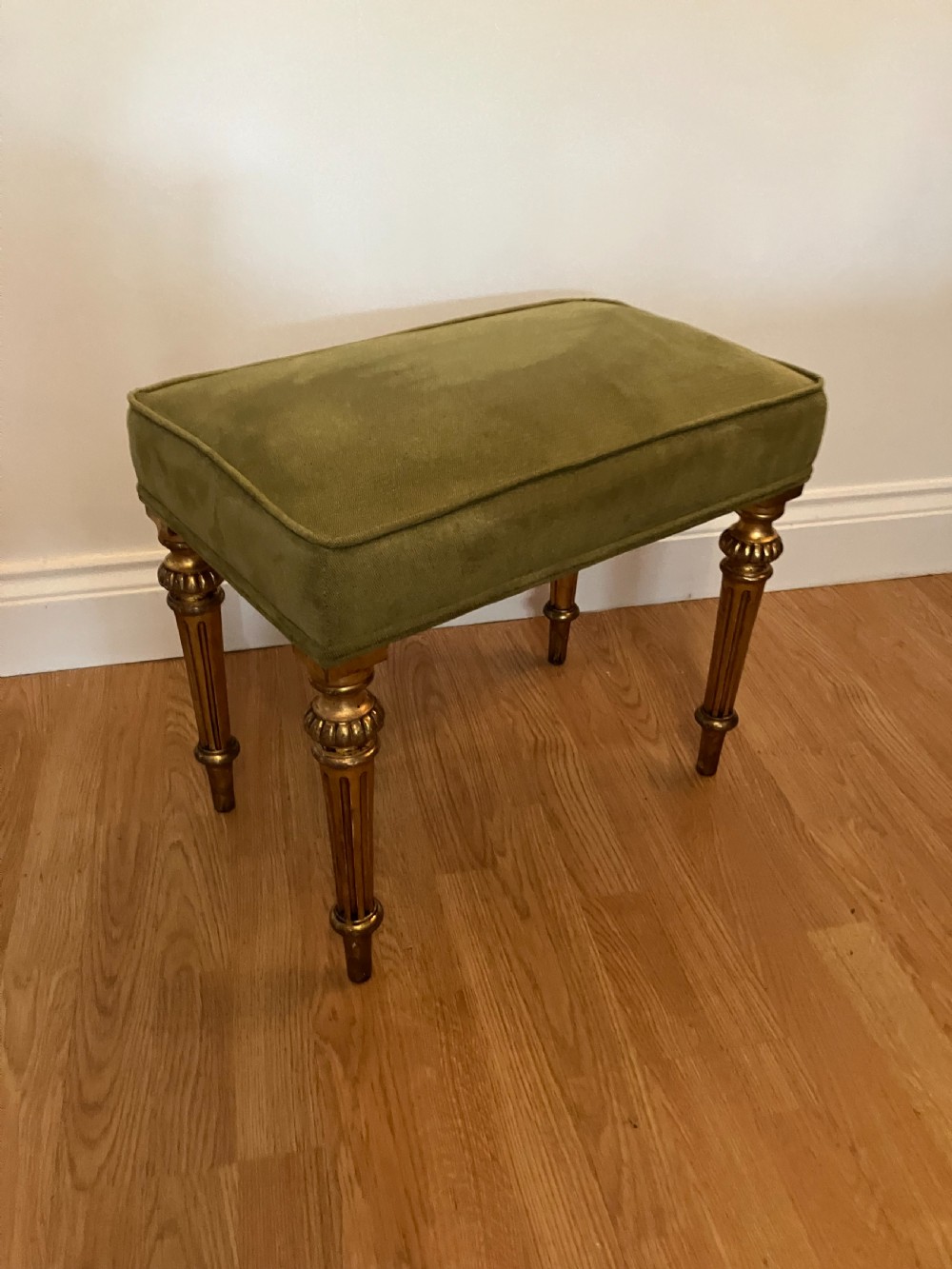 A Victorian giltwood stool featuring fluted gold legs and an olive green velvet padded top.