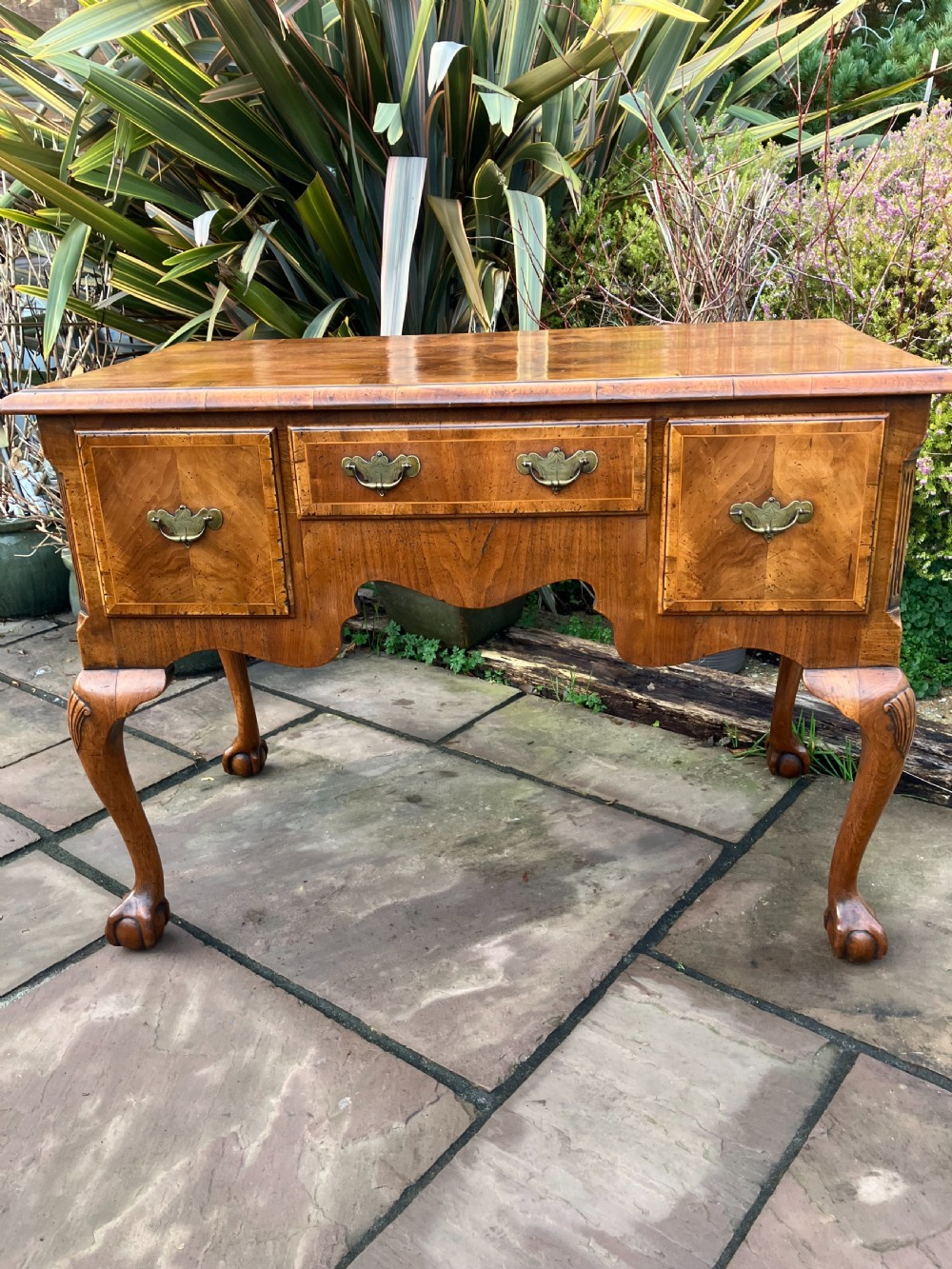 A Queen Anne style walnut lowboy featuring three drawers, brass drop handles, a shaped apron, and cabriole legs ending in ball and claw feet.