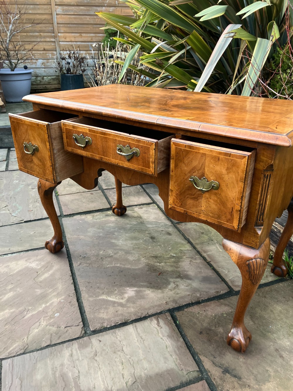 A Queen Anne style walnut lowboy featuring three drawers, brass drop handles, a shaped apron, and cabriole legs ending in ball and claw feet. View II