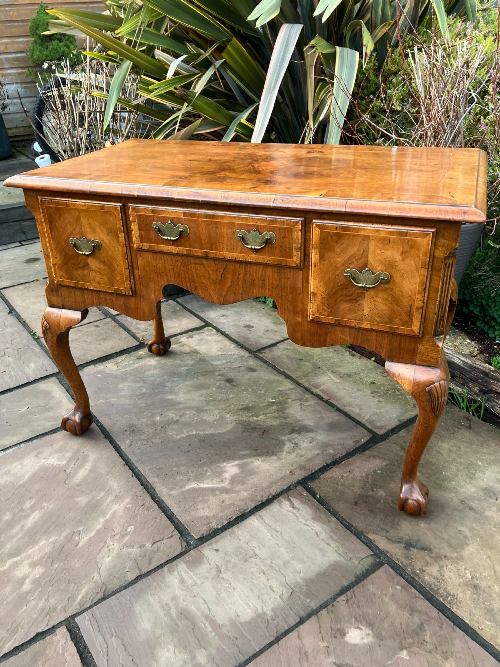 A Queen Anne style walnut lowboy featuring three drawers, brass drop handles, a shaped apron, and cabriole legs ending in ball and claw feet. View VI