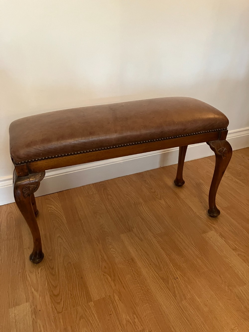 An Edwardian rectangular piano stool featuring brown leather upholstery with stud trimming and timber cabriole legs.