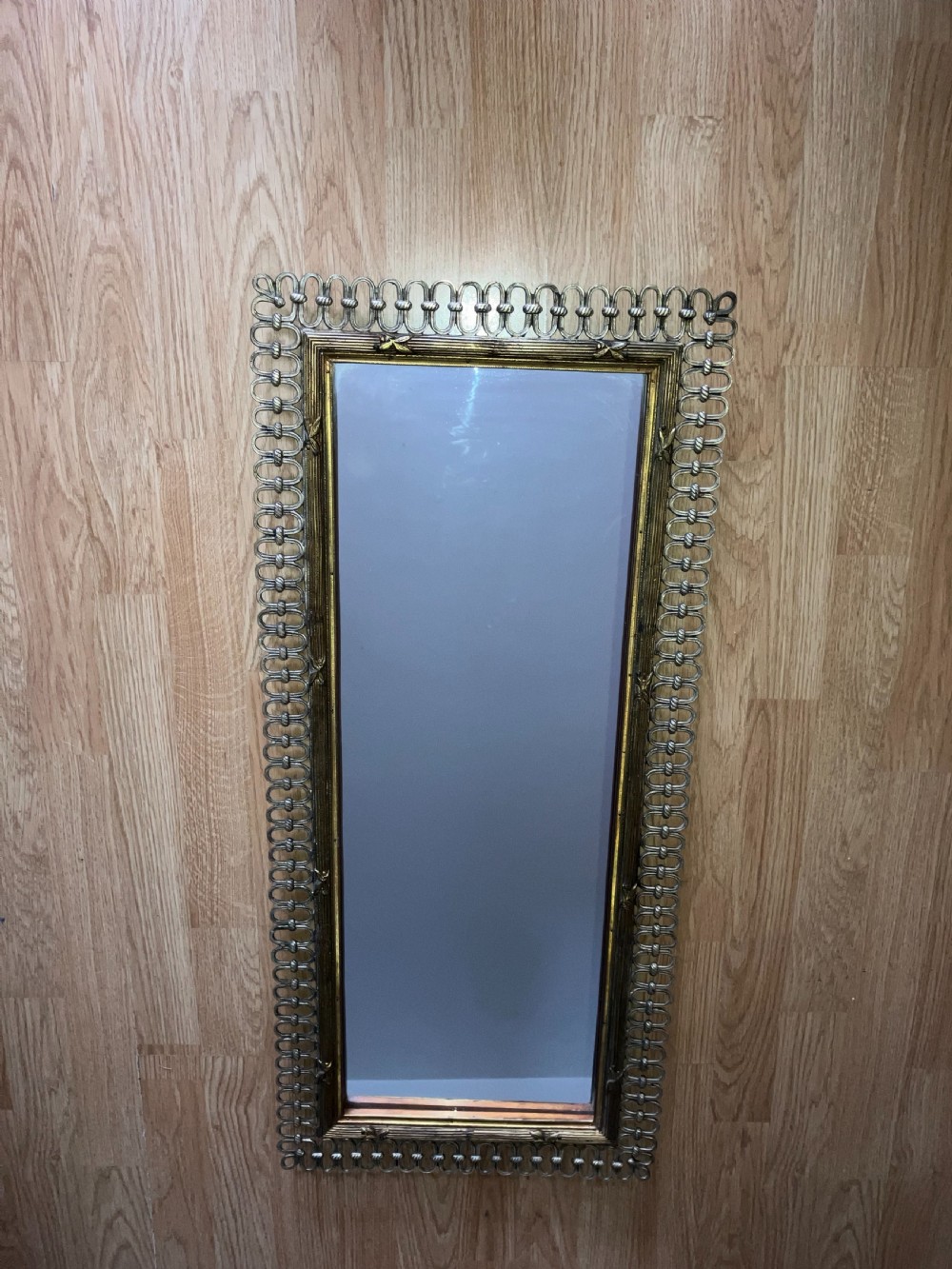 A tall rectangular French wall mirror featuring a gilded inner moulding frame surrounded by an openwork looped metal border.
